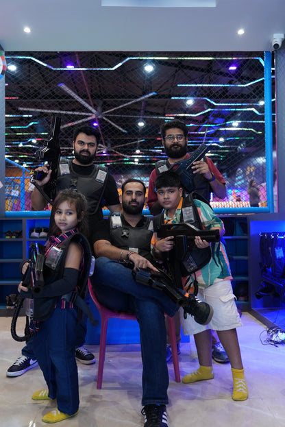 A family poses with laser tag gear and guns in a dimly lit, neon-lit arena.