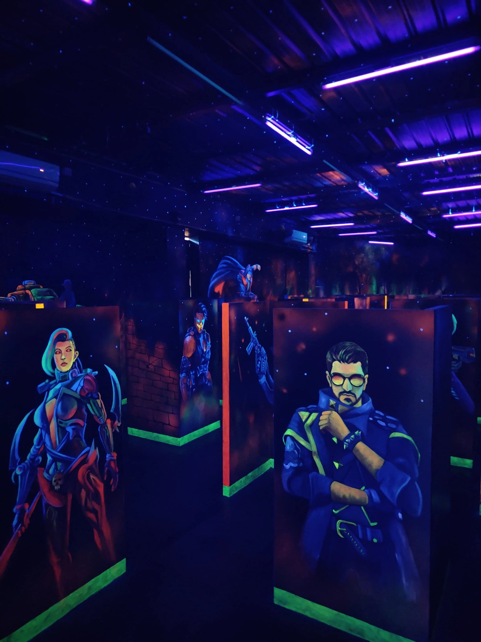 A dimly lit laser tag arena with neon lights and murals of futuristic characters.