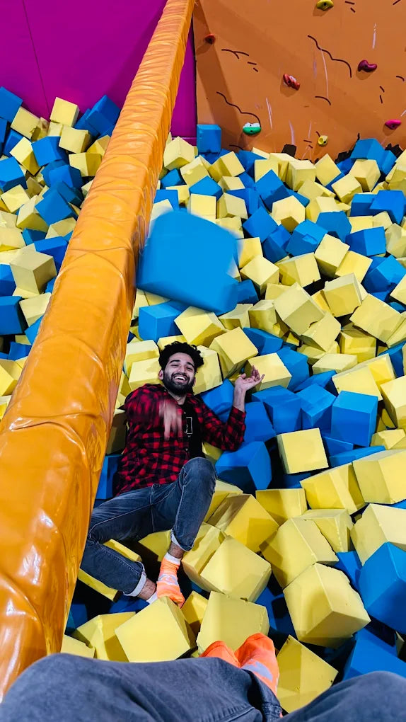 A young man smiles while lying in a foam pit at an indoor playground.