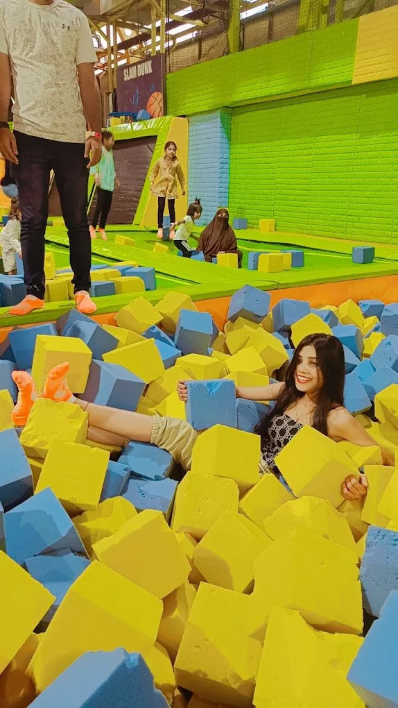 A young woman smiles while lying in a foam pit at a trampoline park.