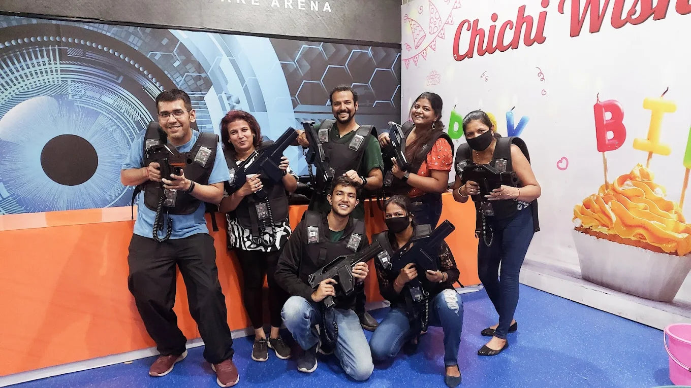 A group of young adults in laser tag vests and holding phasers pose for a photo in a brightly decorated arena.