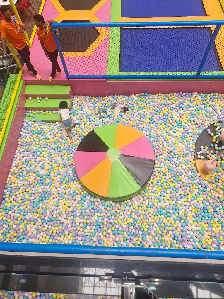 Children playing in a colorful indoor playground with a large wheel of fortune in the center.