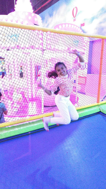 A young girl jumps on a trampoline in a brightly lit indoor play area.