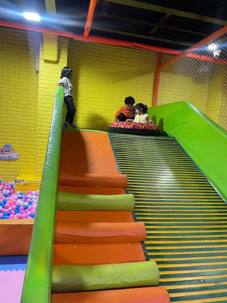 Children play on a colorful indoor playground slide and ball pit.