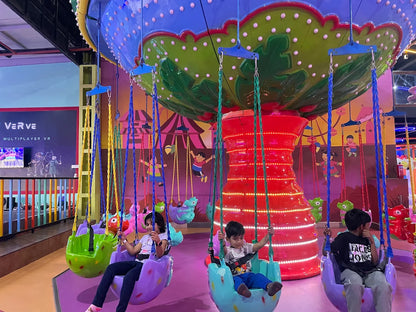 Children ride colorful swings on a carousel ride in an indoor amusement park.