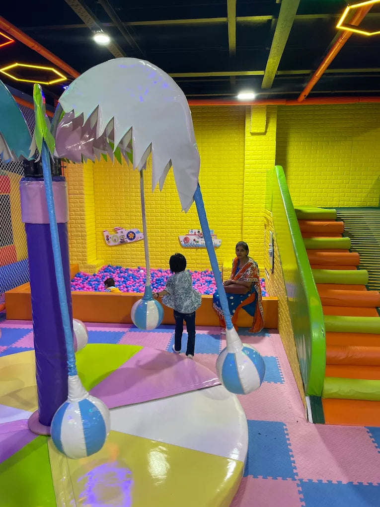 Children play in a colorful indoor playground with a ball pit and soft play structures.