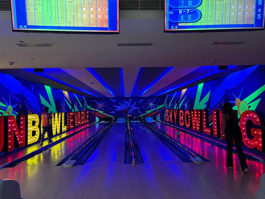 A neon-lit bowling alley with large illuminated signs and two young adults.