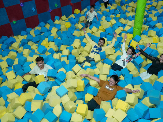 Group of people having fun playing and relaxing in a large foam pit filled with blue and yellow cubes indoors