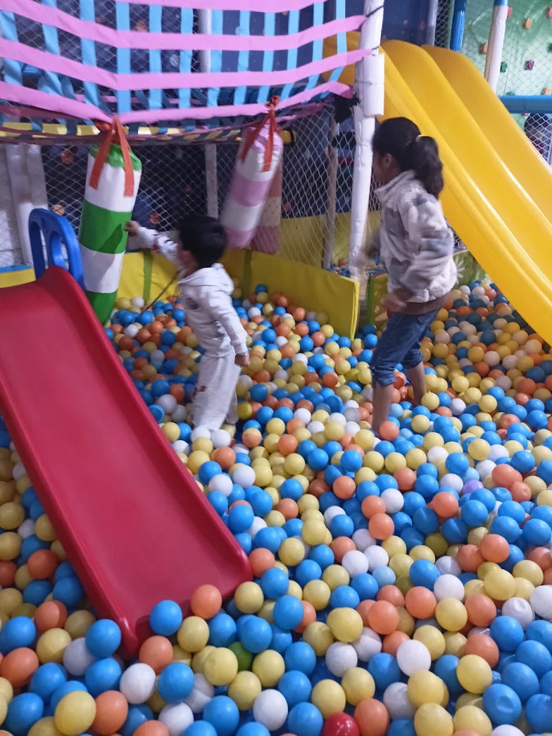 Children play in a ball pit with slides and punching bags at an indoor playground.