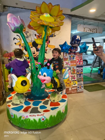 A young child rides a colorful amusement park ride with cartoon characters, while another child sits nearby.