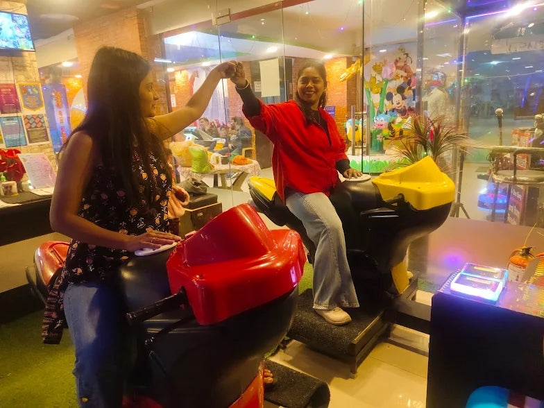 Two young women play on motorcycle arcade games in an amusement center.