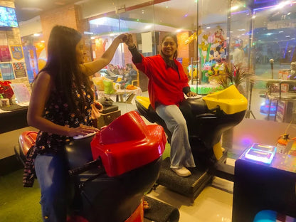 Two young women play on motorcycle arcade games in an amusement center.