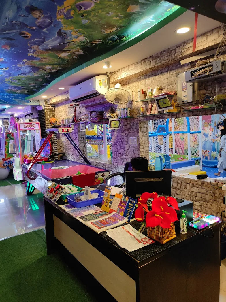 An indoor play area with arcade games, an air hockey table, and a reception desk. A person is visible behind the desk.