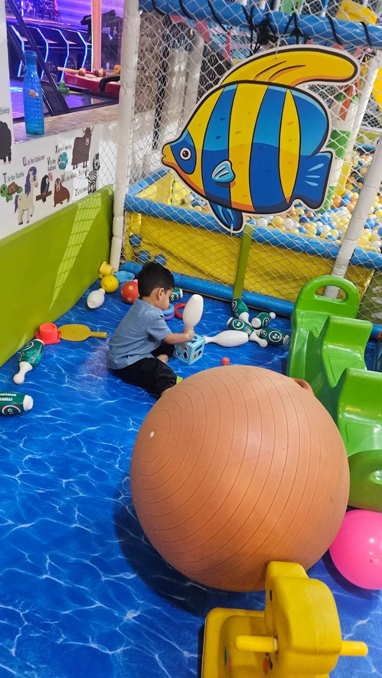 A young boy plays with toys in a colorful indoor play area with a ball pit.