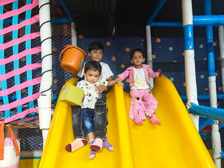 Children play on a yellow slide in a colorful indoor playground.
