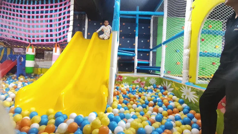 A child sits on a yellow slide in a ball pit at a playground.
