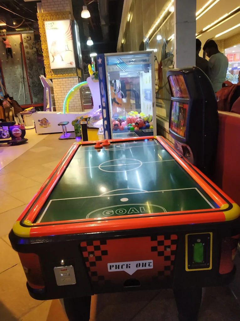 An air hockey table in an arcade with a claw machine and other games in the background.