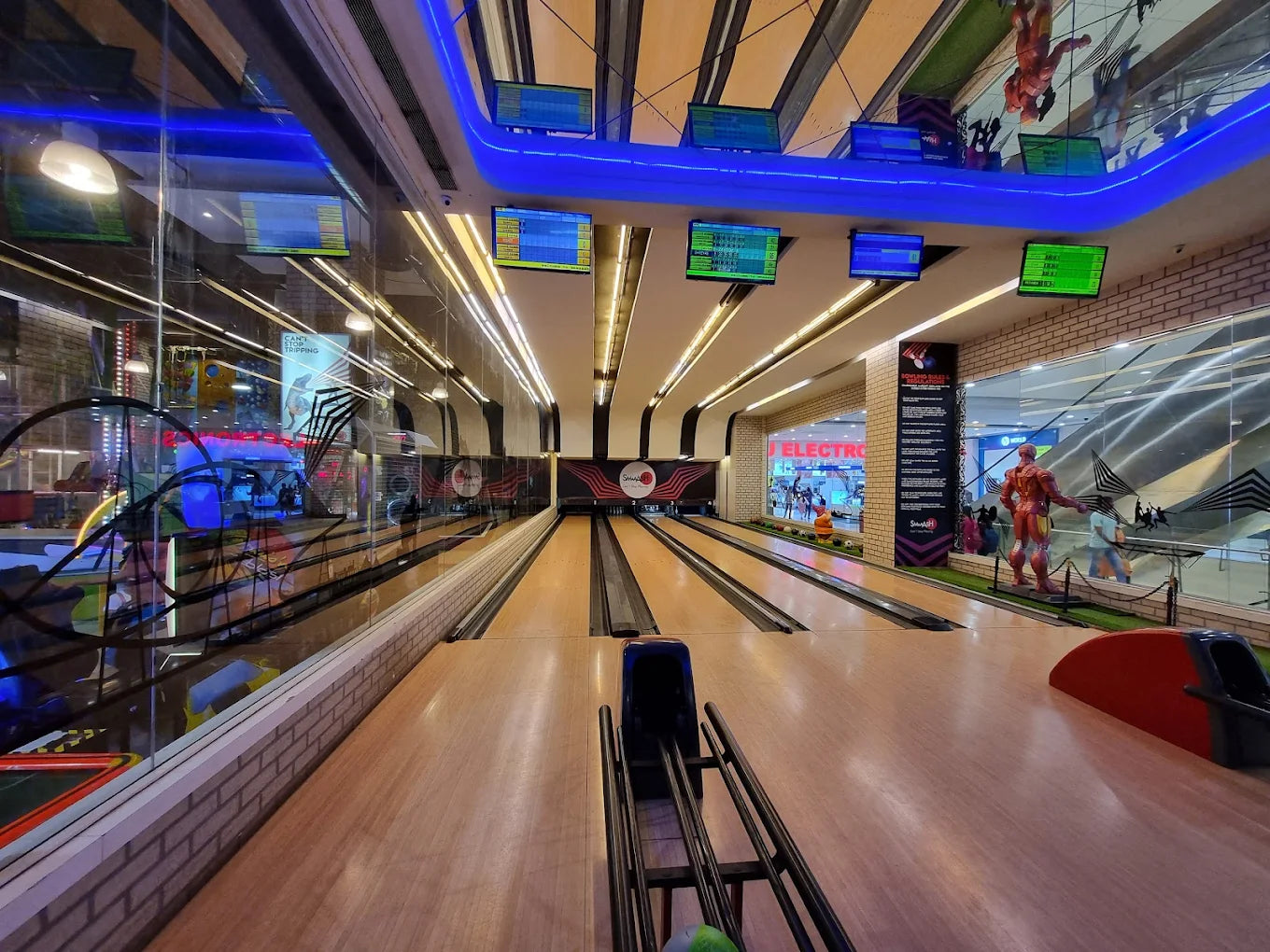 A bowling alley with multiple lanes, illuminated by blue and white lights, with people visible in the background.