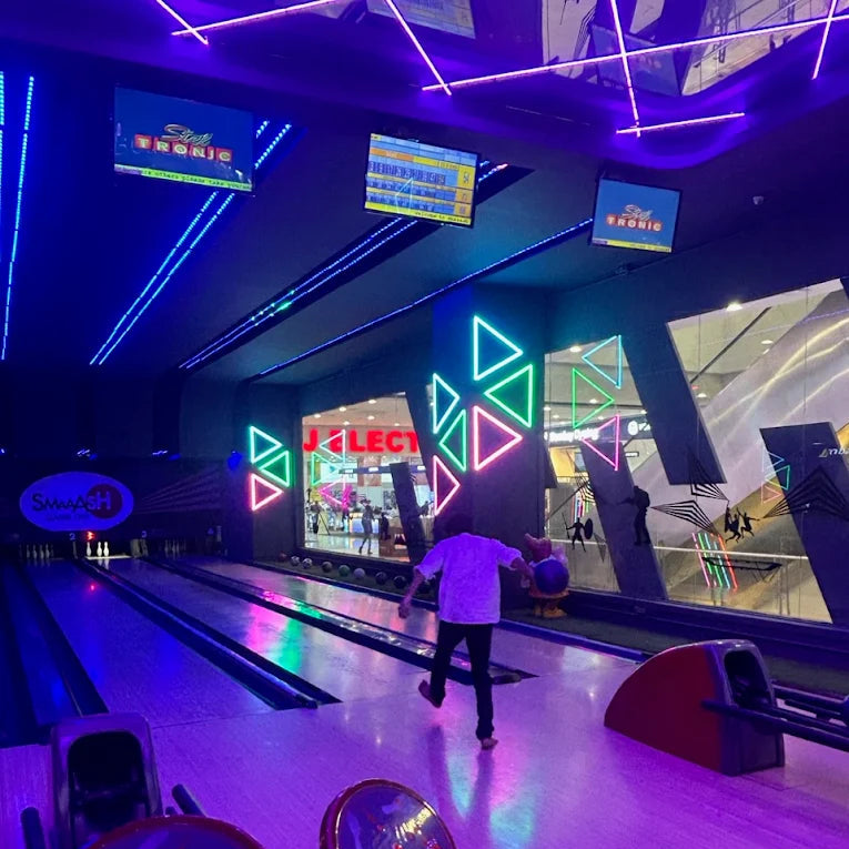 A person bowls in a neon-lit entertainment center with bowling lanes and screens.
