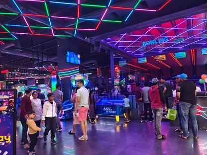 People of various ages enjoy an arcade with neon lights and games like bowling and air hockey.