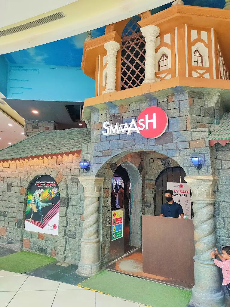 A young child and a man stand near the entrance of a themed entertainment center called Smaaash.