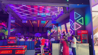 People bowling and playing games in a brightly lit arcade with neon lights.