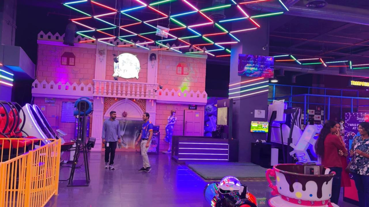 An indoor amusement park with neon lights, arcade games, and young adults.