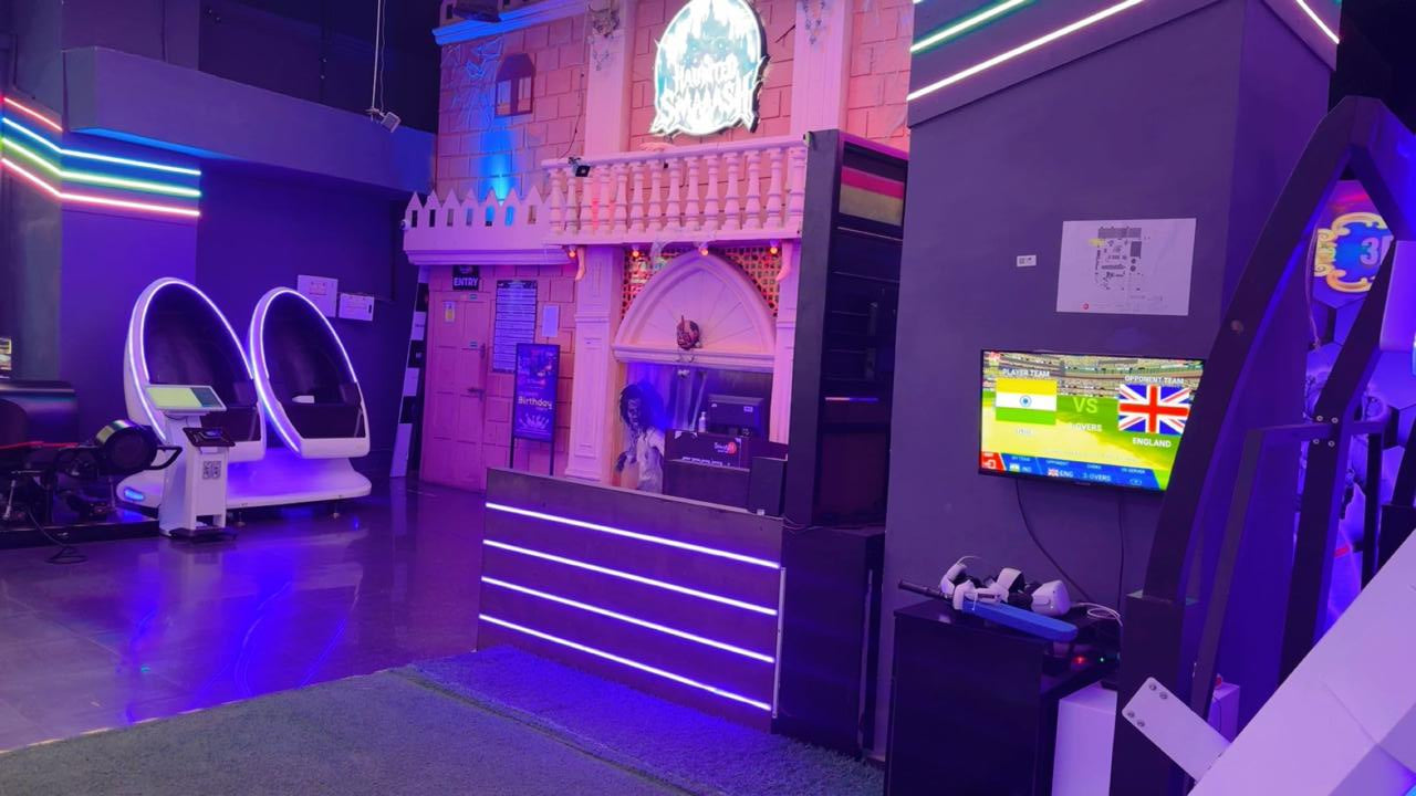 An indoor entertainment venue with VR pods, a cricket game on screen, and neon lights.