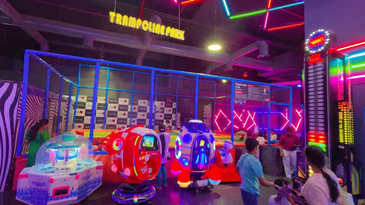 Neon-lit indoor trampoline park with arcade games and children playing.