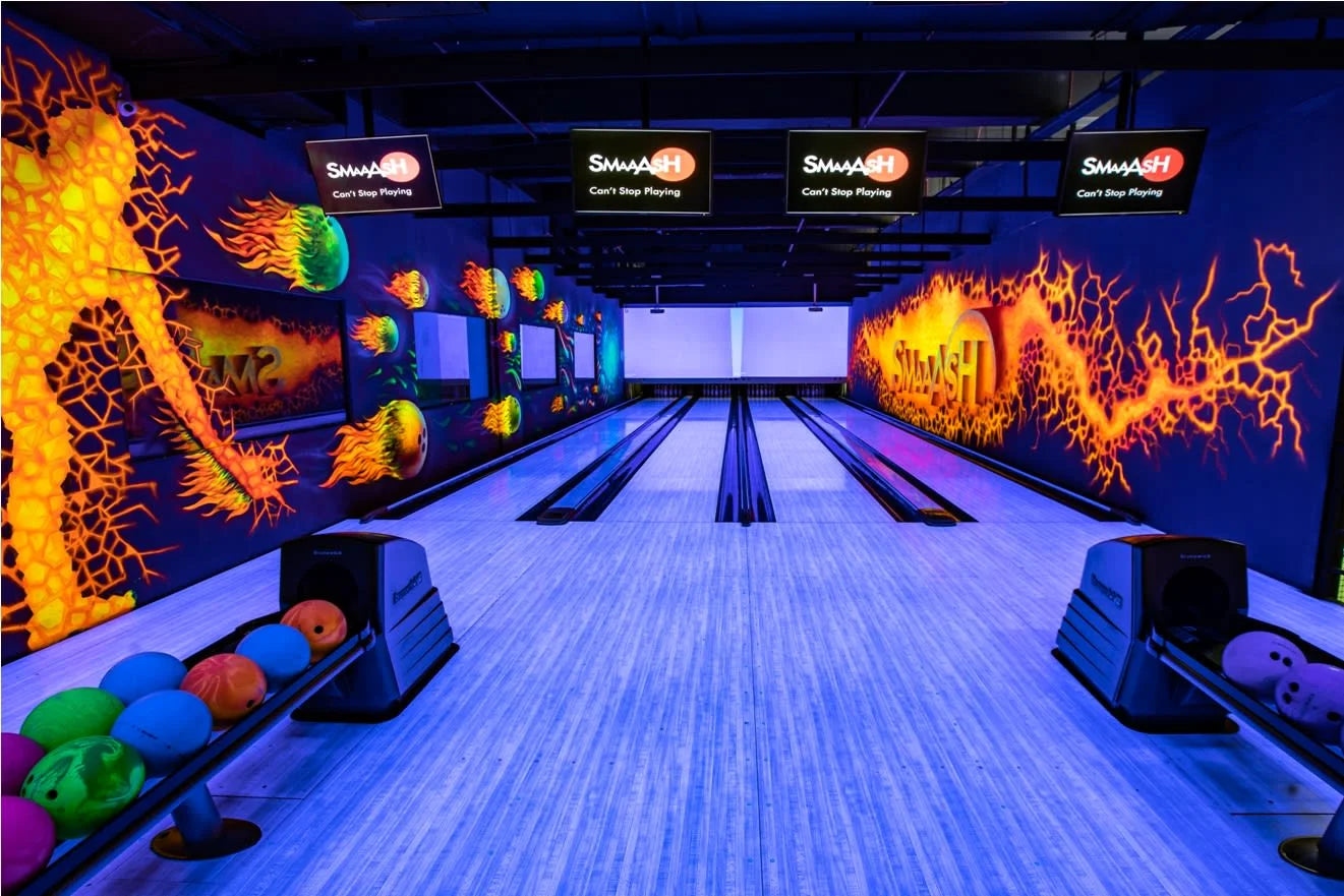 A neon-lit bowling alley with vibrant, glowing murals and bowling balls ready for play.