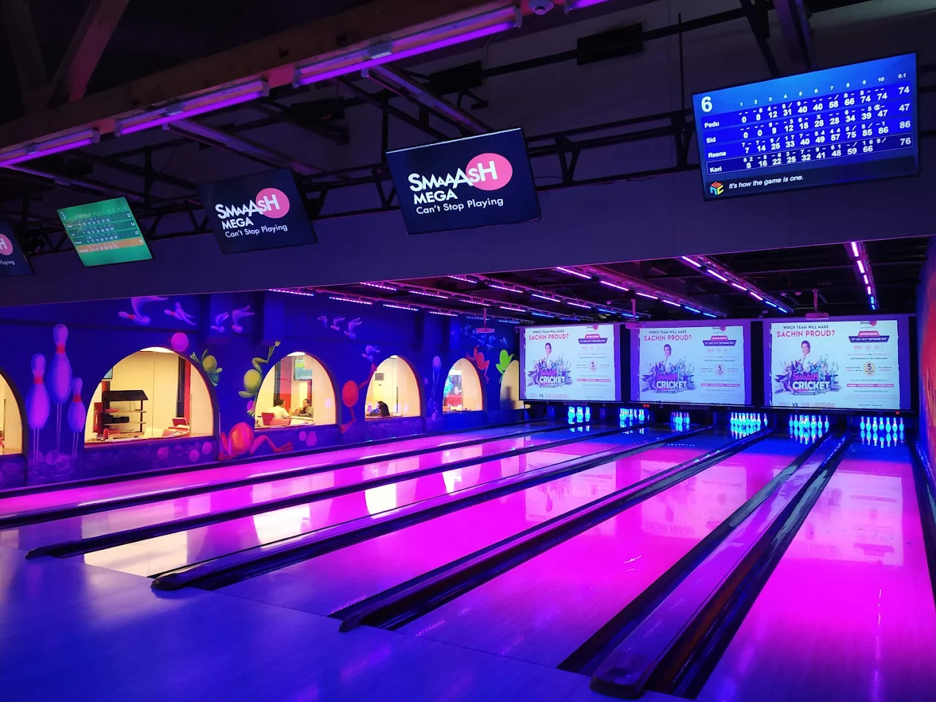A bowling alley with neon lights and a scoreboard showing scores for players.