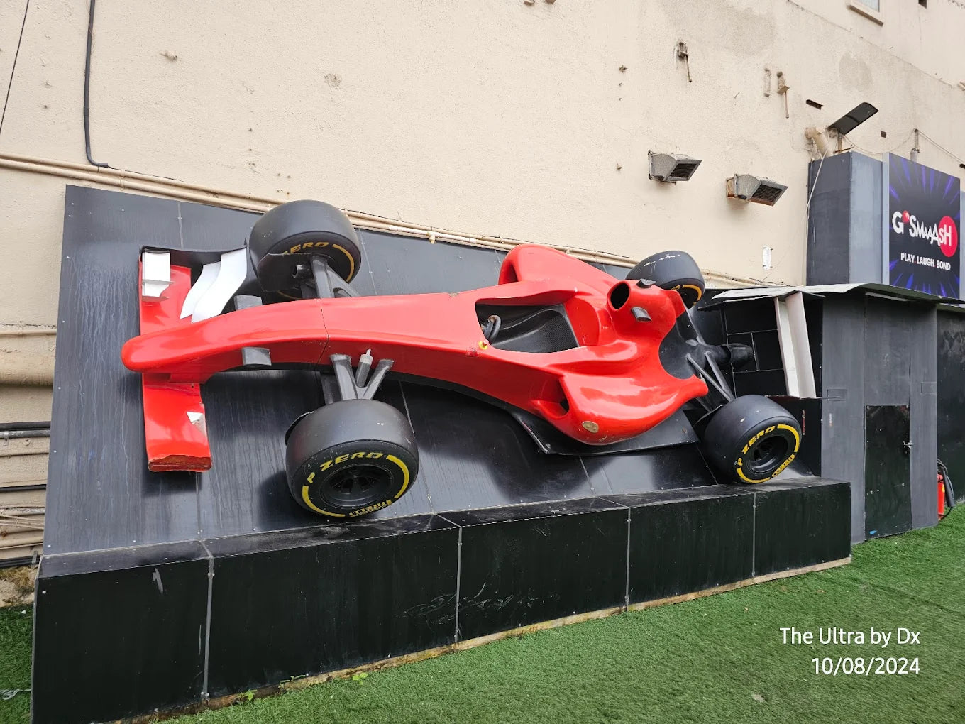 A red Formula 1 car replica is mounted on a black display, with a sign for "G'SMASH" in the background.