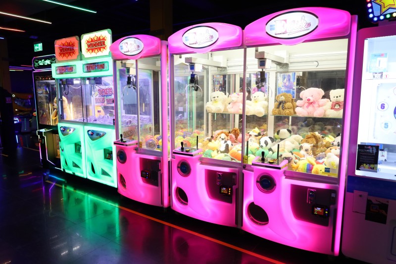 Row of brightly lit arcade claw machines filled with stuffed animals.