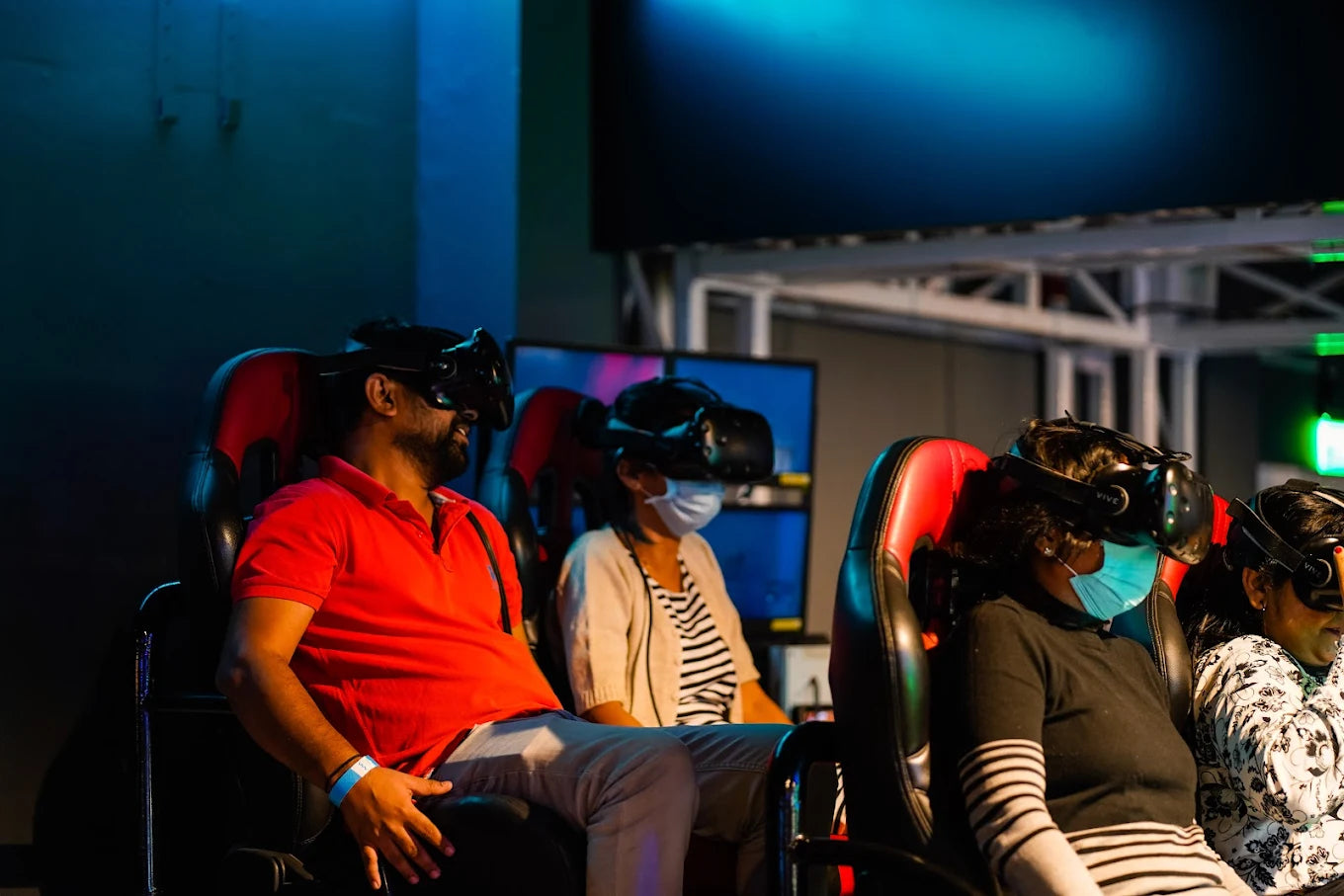 People wearing VR headsets sit in chairs, experiencing a virtual reality simulation in a dimly lit room.