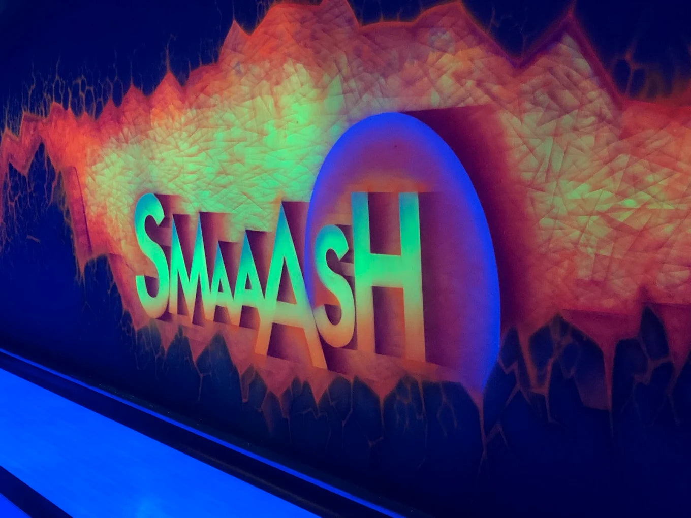 Neon sign for "SMAAASH" in a bowling alley with a fiery background.