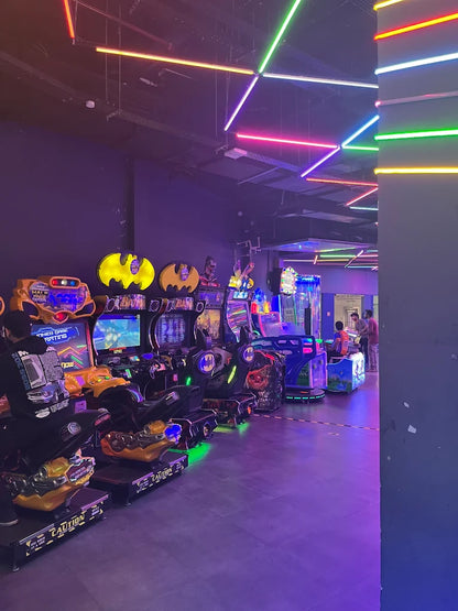Arcade with Batman-themed racing games and neon lights. Young people are playing games in the background.