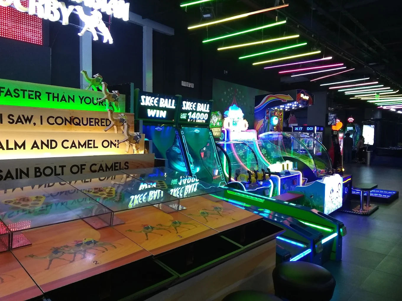 An arcade with Skee-Ball and other games, featuring neon lights and camel-themed decor.