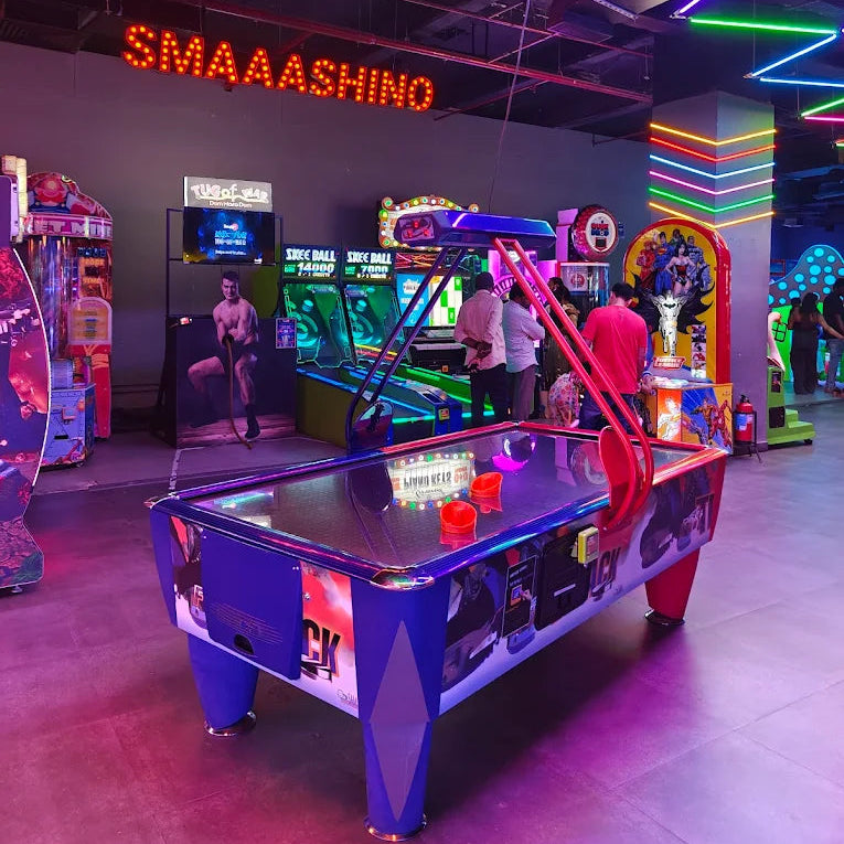 An air hockey table in a brightly lit arcade with people playing games.