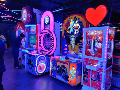 Arcade with glowing games, including a candy crane and Justice League-themed machines, with a person playing a game.