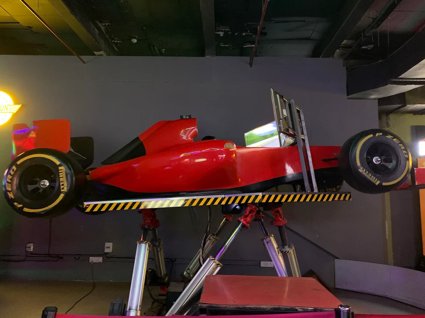 A red F1 racing simulator with screens, mounted on a stand.