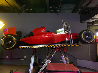 A red F1 racing simulator with screens, mounted on a stand.
