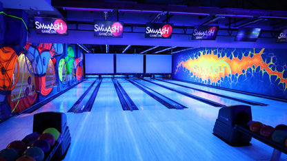 A brightly lit bowling alley with neon lights and colorful murals. Bowling balls are lined up in a rack.