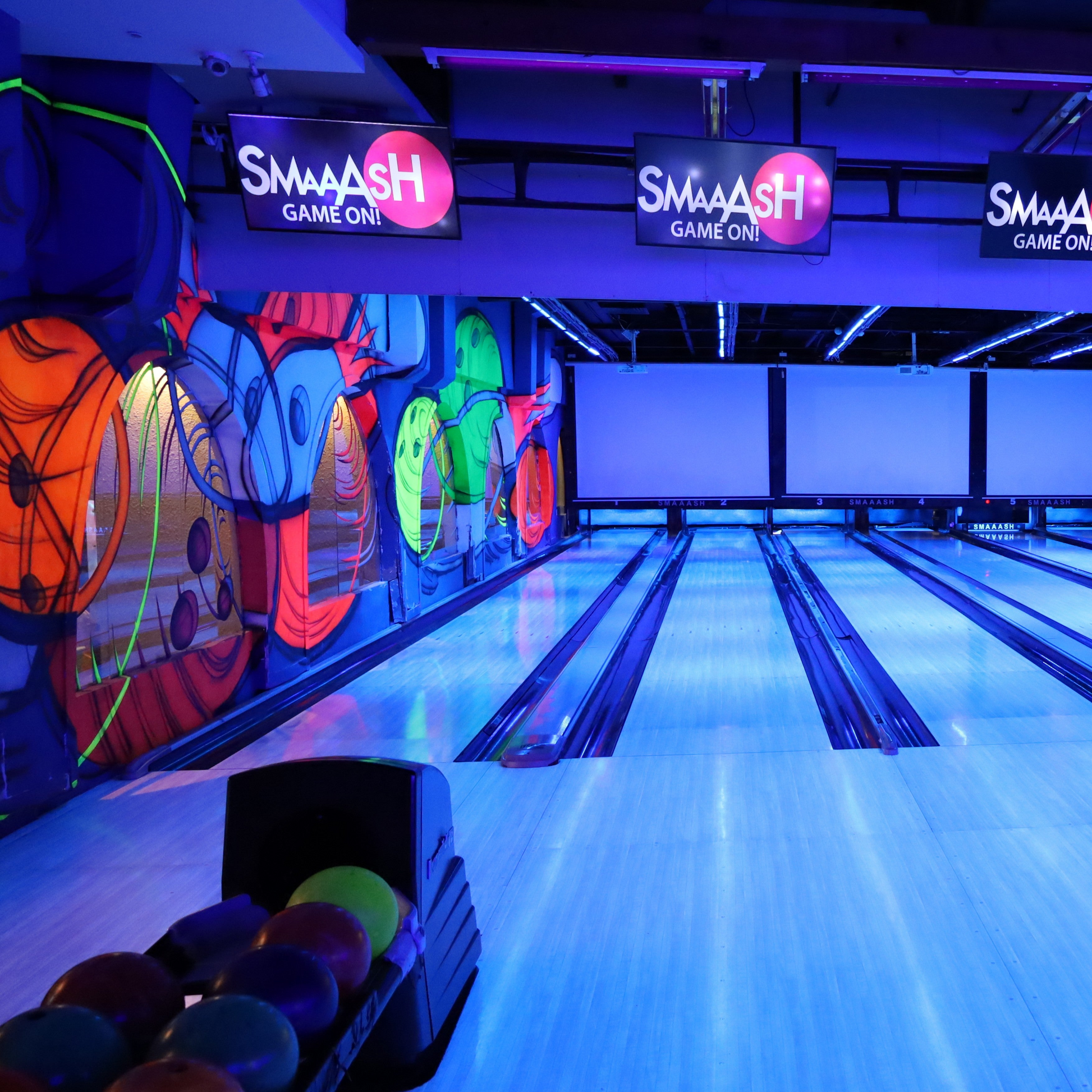 A bowling alley with neon lights and graffiti, featuring bowling balls in the foreground.