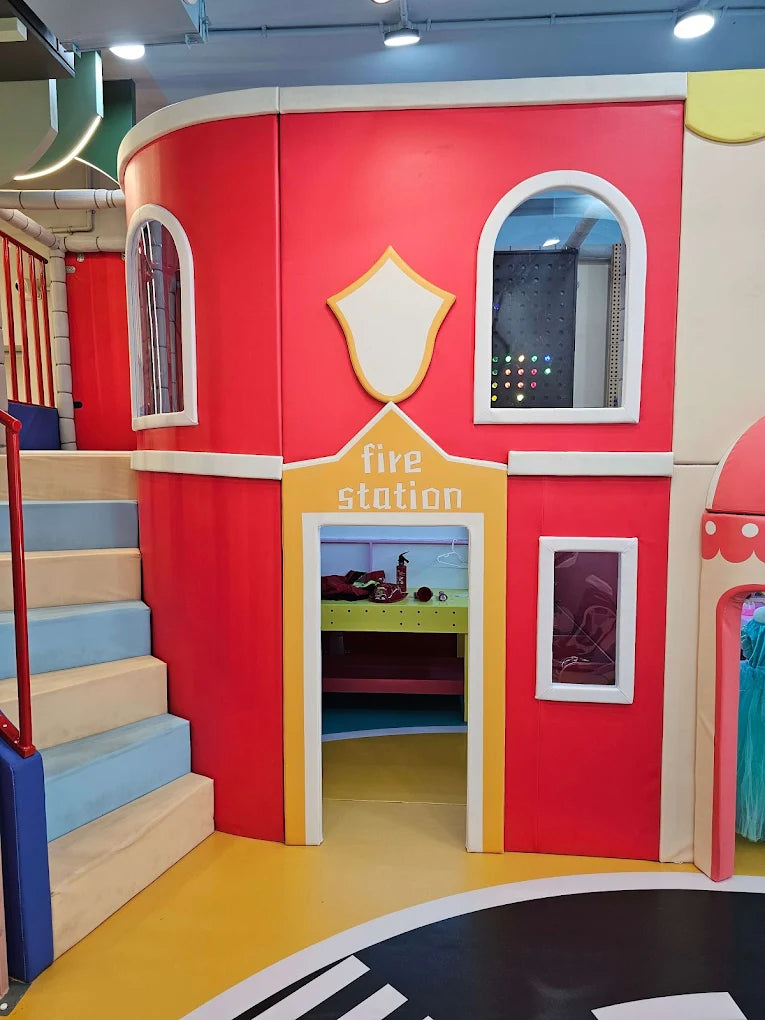 A colorful indoor playground designed as a fire station, with stairs and an open doorway.