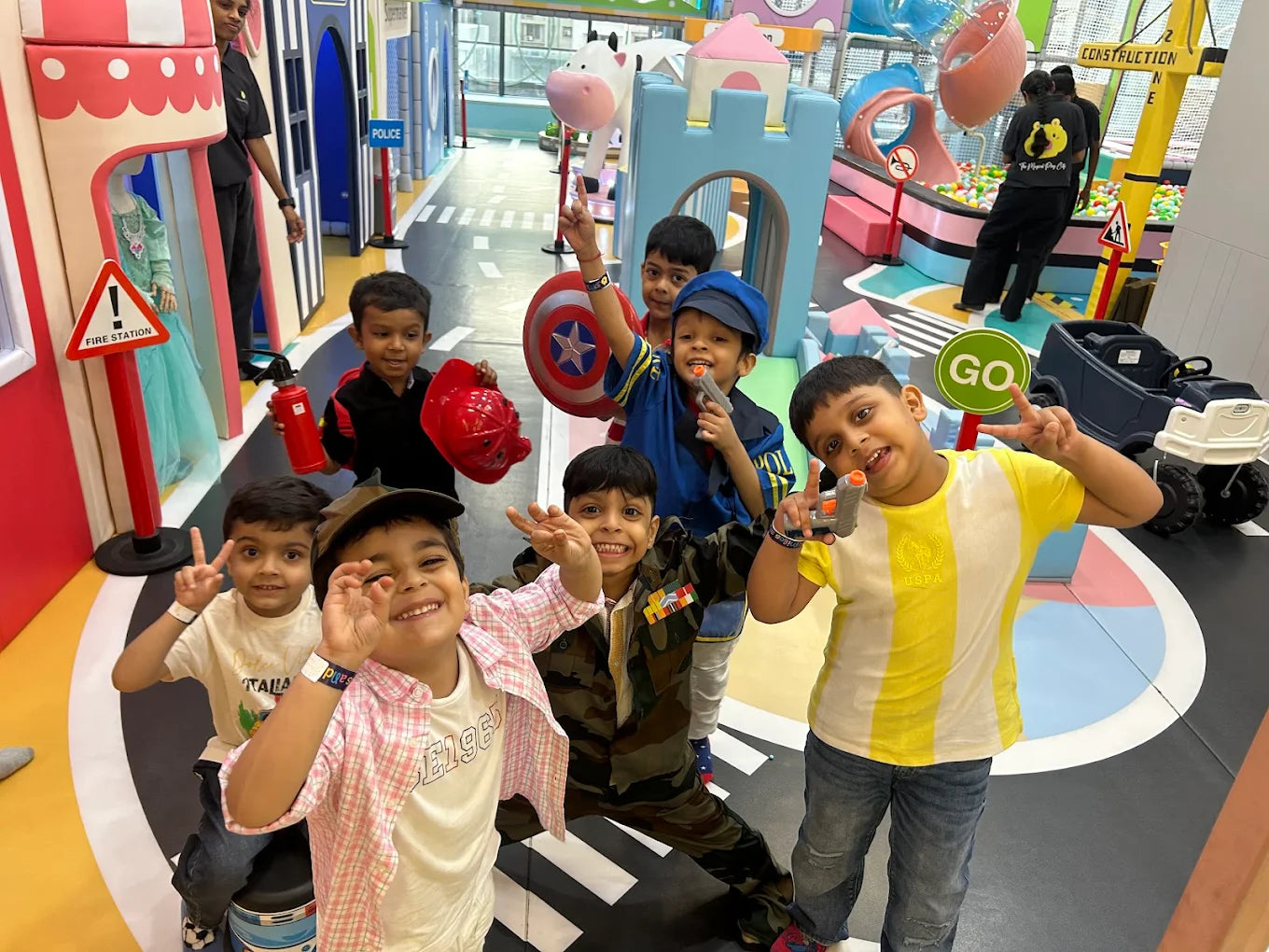 Children in costumes play in a colorful indoor playground with toy guns and props.