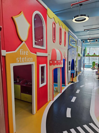 A colorful indoor play area designed like a town with buildings and a road. Children can pretend to be firefighters or police officers.