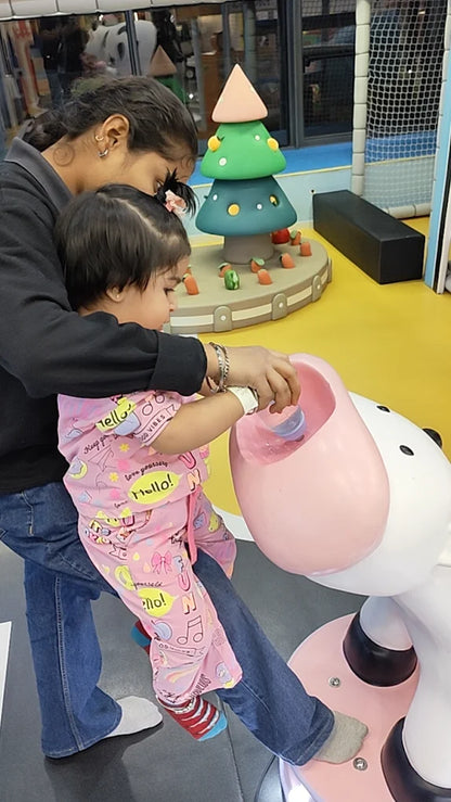 A young child plays with water in a pink toy while a woman holds them in a colorful indoor play area.