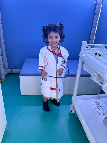 A young child dressed as a doctor with a stethoscope smiles in a room with blue walls.