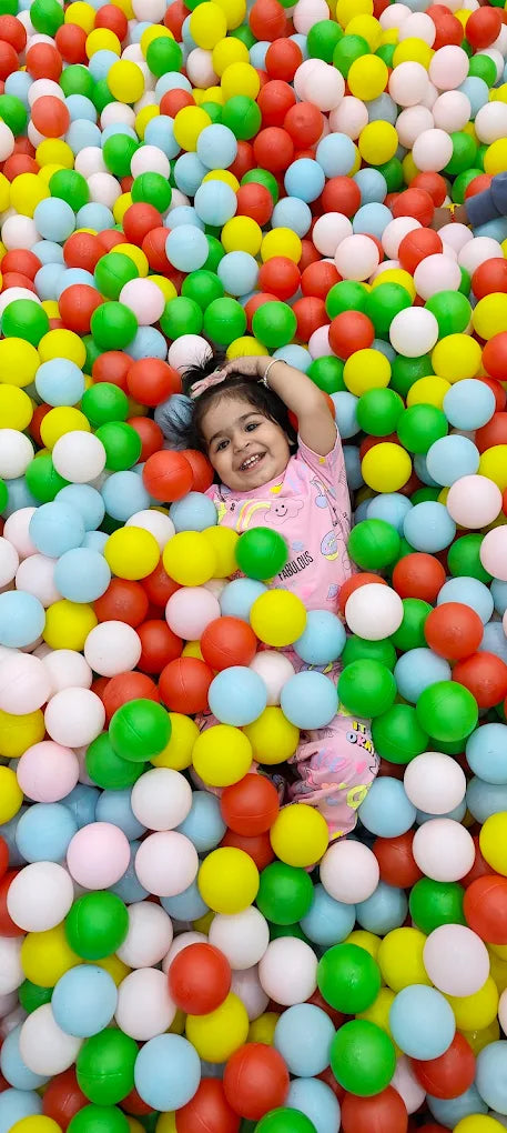 A young child smiles while playing in a ball pit filled with colorful balls.
