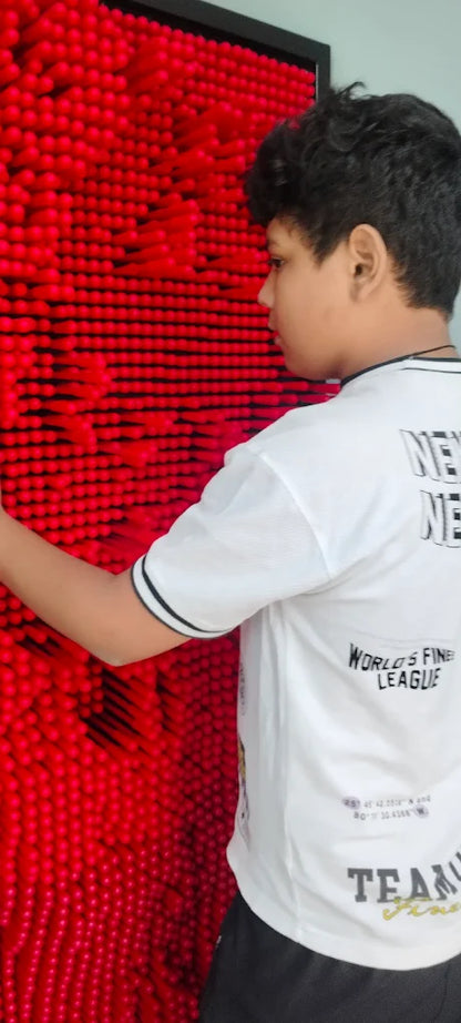 A young person interacts with a red pin art toy, creating a 3D impression.